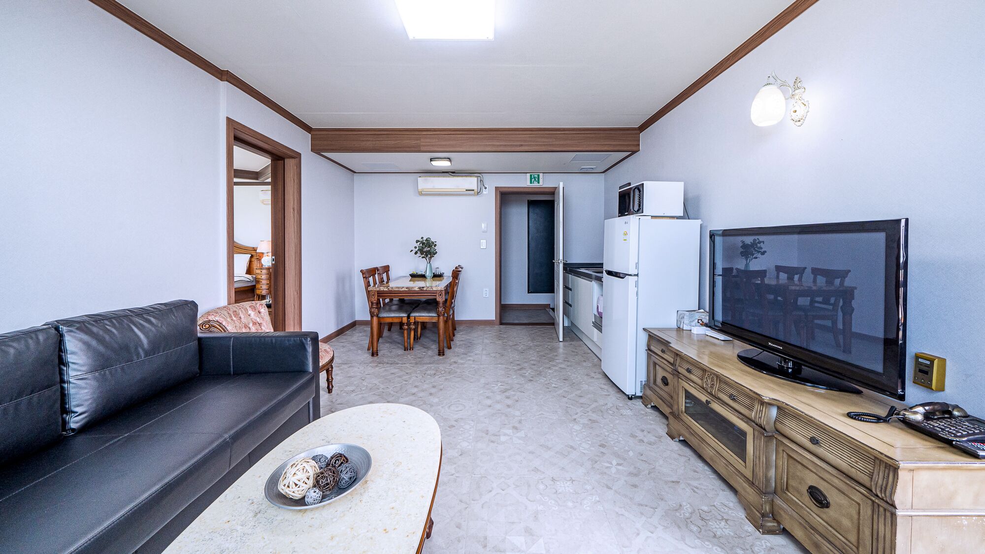 A living room with a sofa, a dining table with chairs, a television, and a refrigerator.