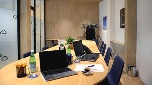 A conference room with a long table, laptops, chairs, and a plant. - Air Rooms Rome Airport by HelloSky (Fiumicino)