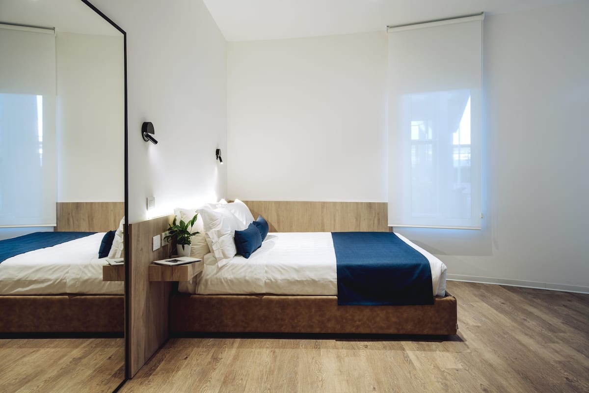 A modern bedroom with a wooden bed, a bedside table, a mirror, and a window.
