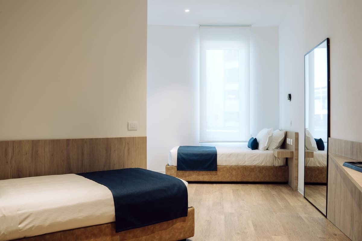 A modern hotel room with two beds, a large window, and a mirror.