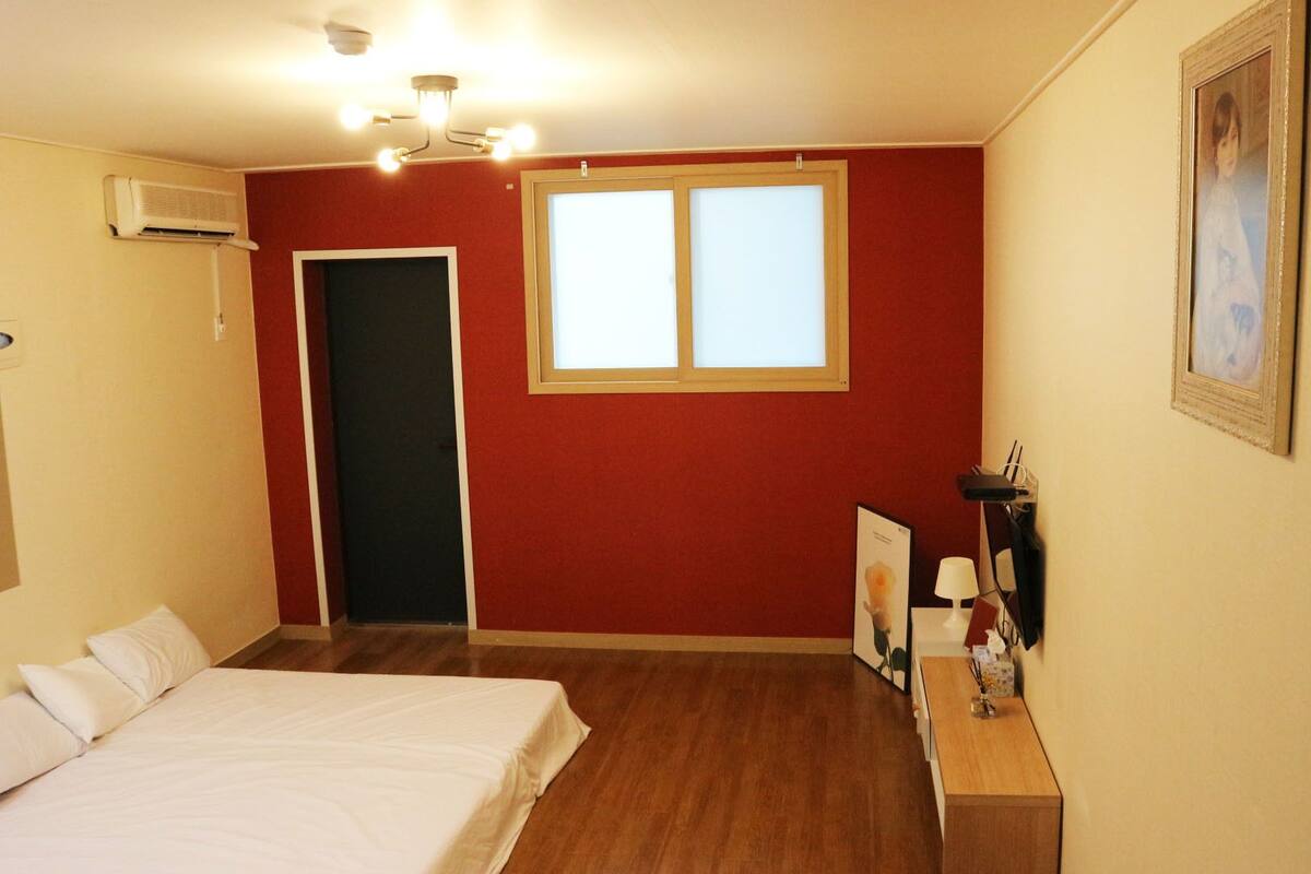 Hotellihuone, jossa on sänky, työpöytä, tuoli, ikkuna ja ilmastointilaite.