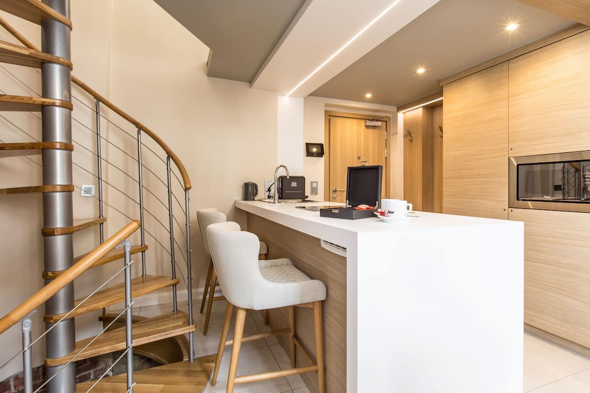 A modern kitchen with a central island, wooden staircase, and a built-in oven.