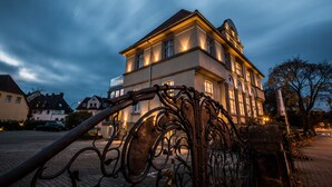 A large building with multiple windows and a balcony, surrounded by a metal fence. - Adelhoff (Osnabrueck)