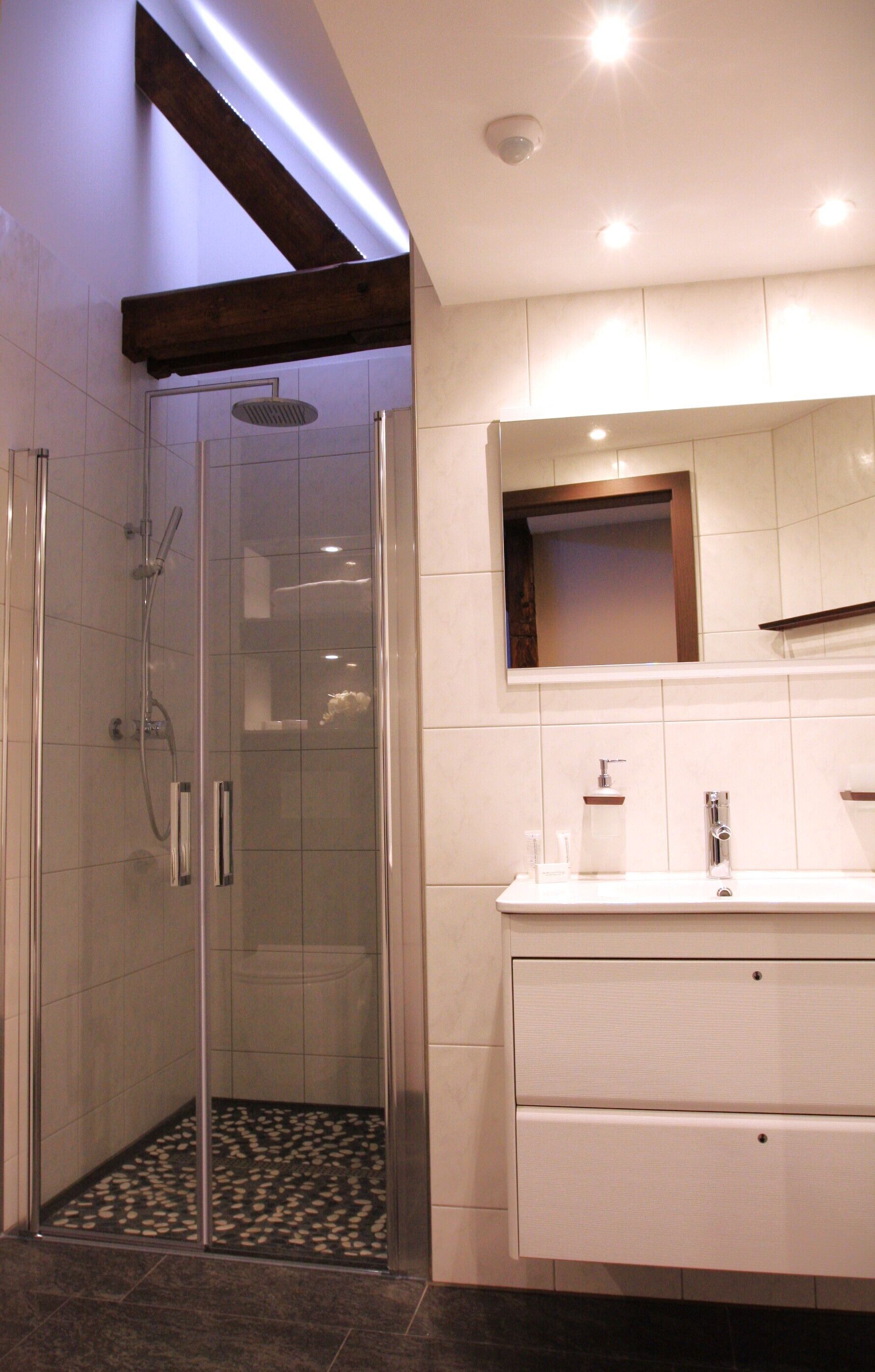 Een moderne badkamer met een douchecabine van glas, een witte wastafel met spiegel en een betegelde vloer.