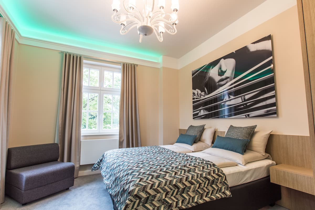 A modern bedroom with a large bed, a side table, a sofa, and a window with curtains.