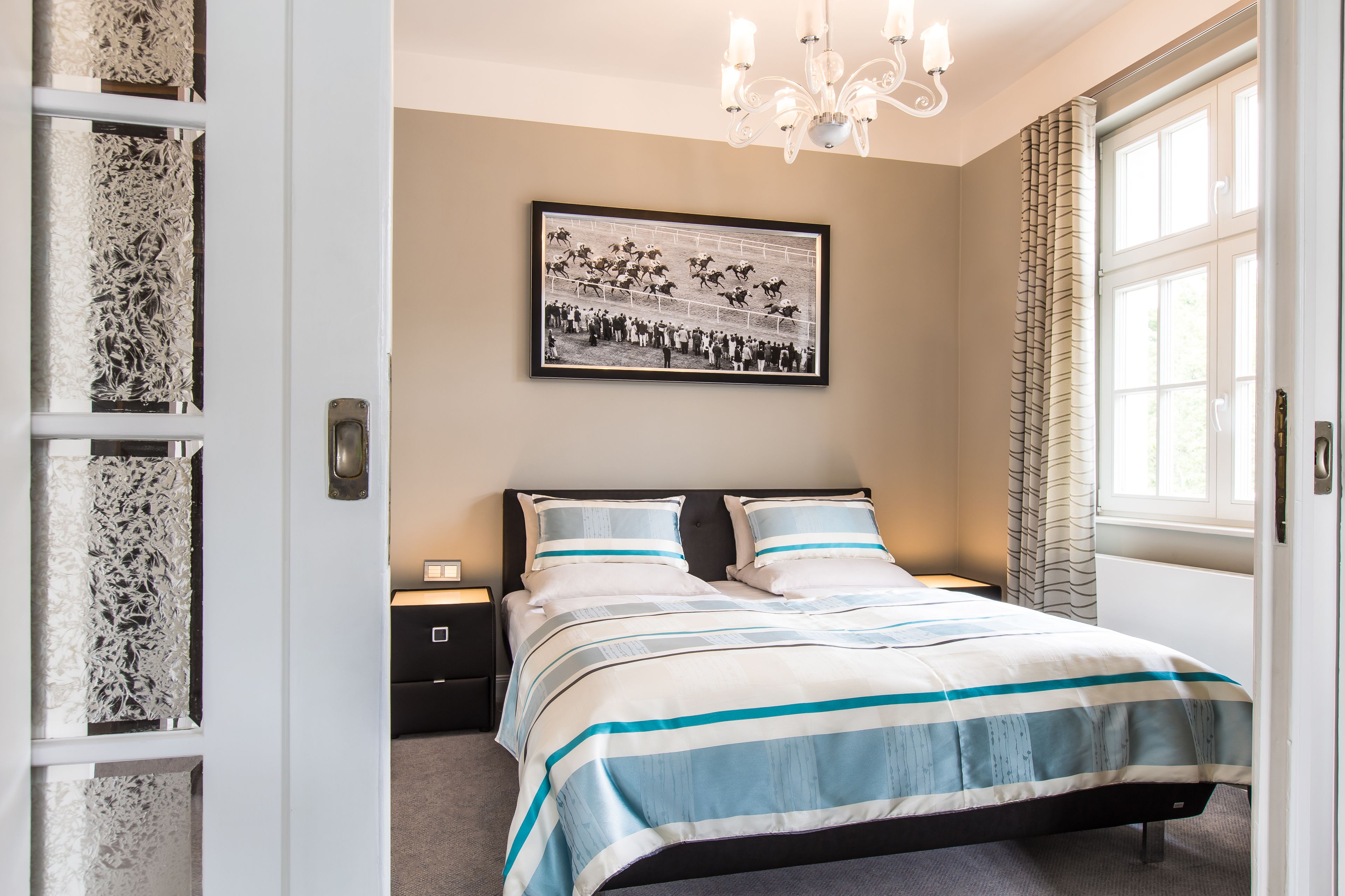 A bedroom with a bed, a nightstand, a framed picture on the wall, and a window with curtains.