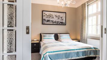 A bedroom with a bed, a nightstand, a framed picture on the wall, and a window with curtains.