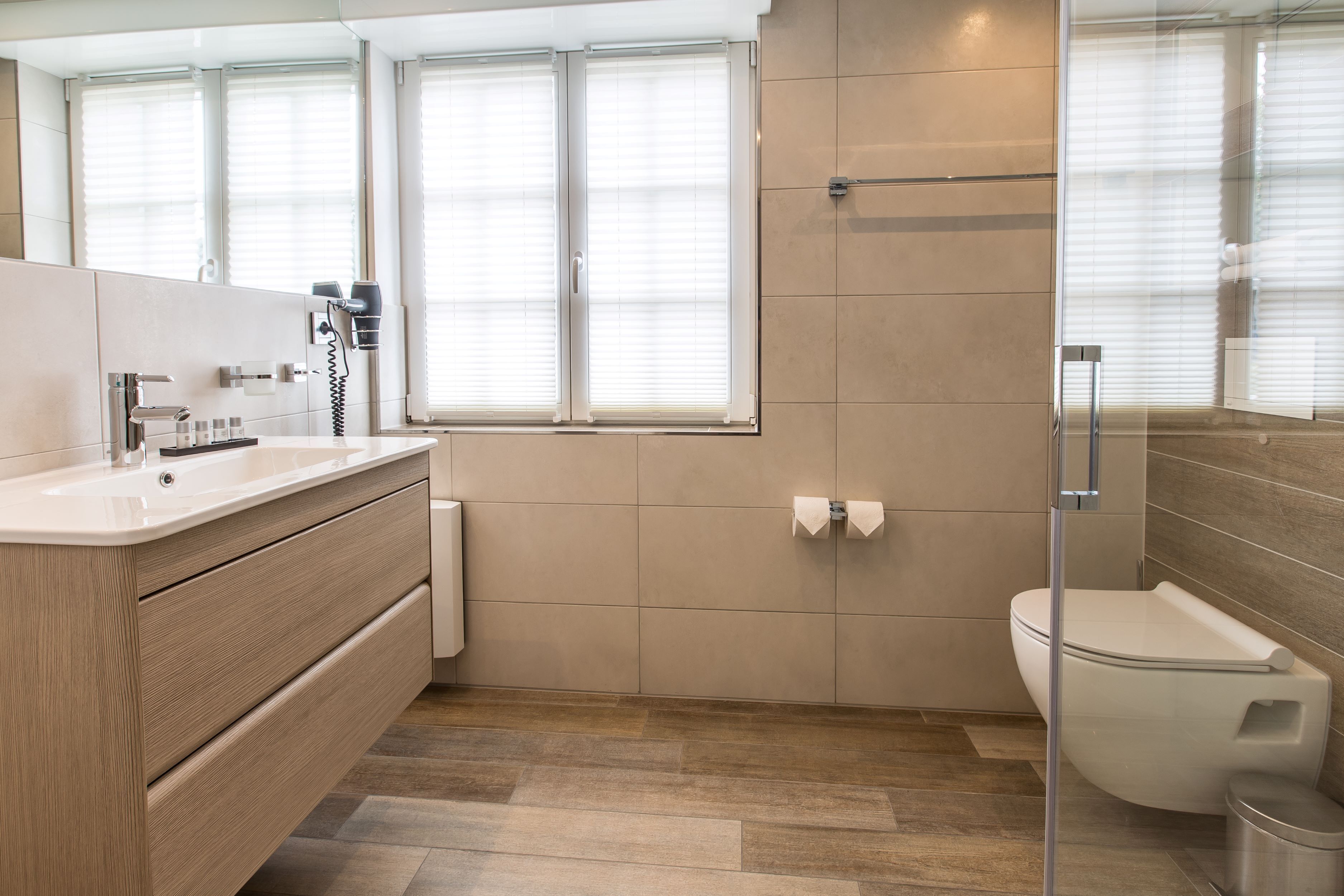 Une salle de bain moderne avec un meuble-lavabo en bois, des toilettes et une douche à parois de verre.
