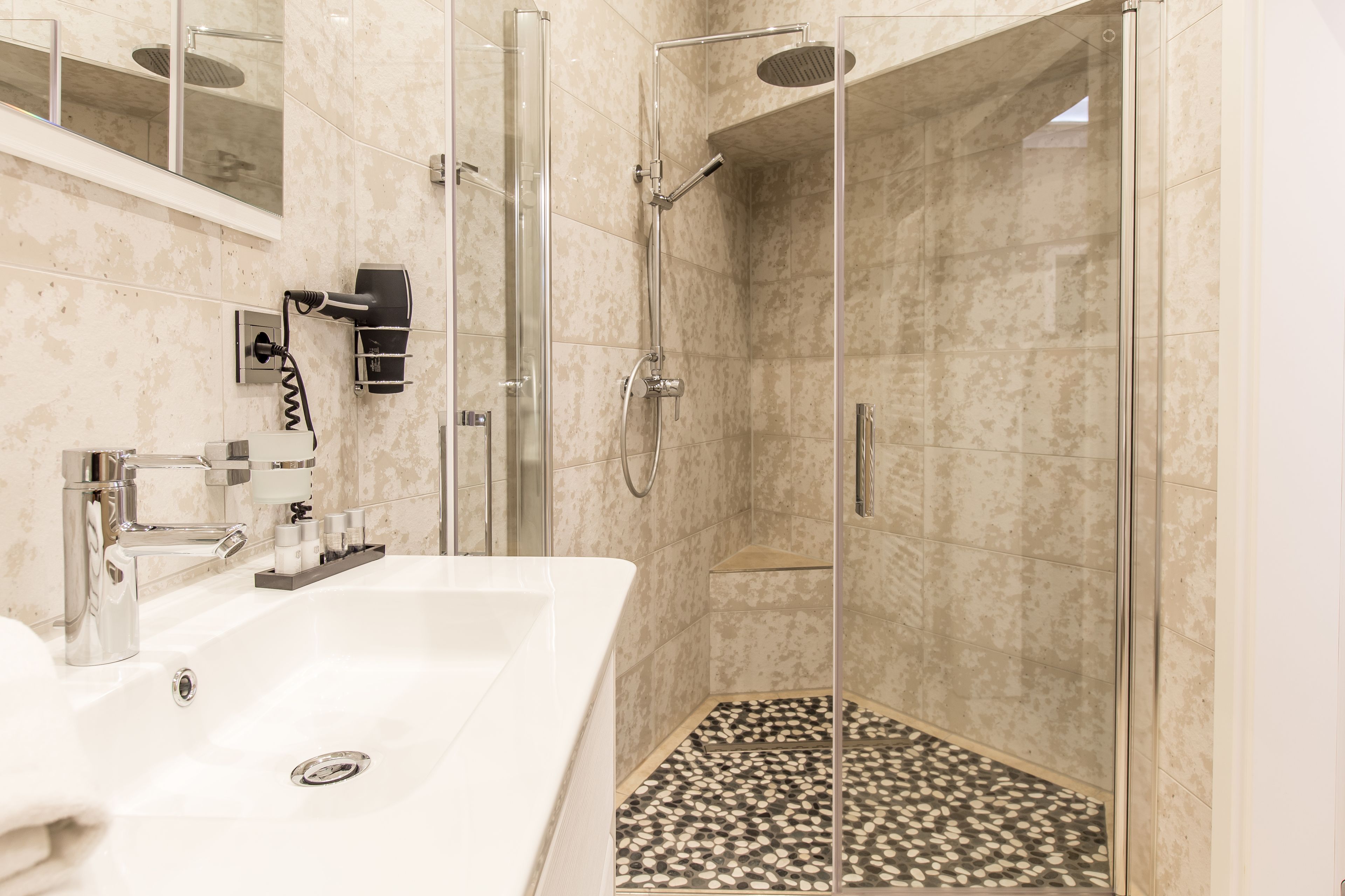 A modern bathroom with a glass-enclosed shower, a white sink, and a tiled floor.