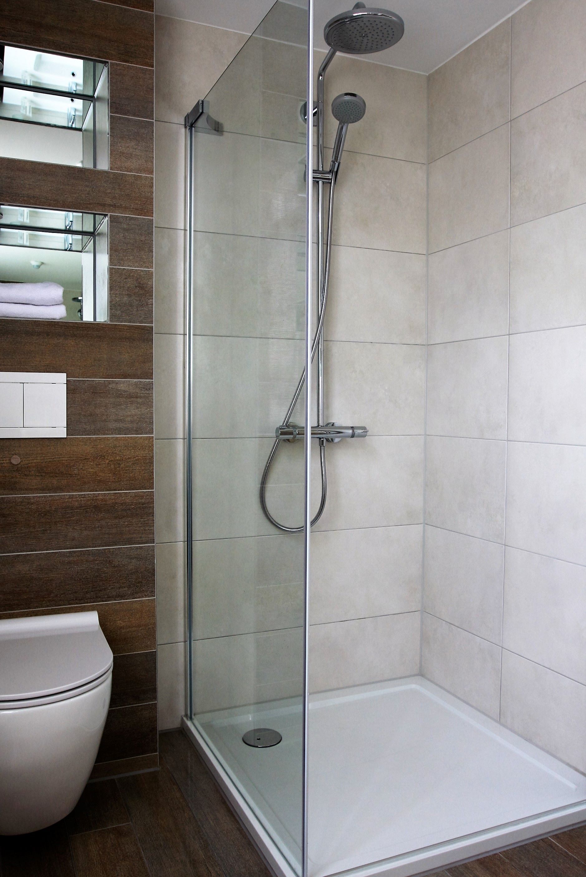 Une douche moderne avec une porte en verre, des toilettes blanches et un lambris en bois sur le mur.
