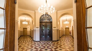 A hotel lobby with a checkered floor, a grand chandelier, and arched doorways. - Adelhoff (Osnabrueck)