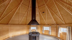 A spacious wooden cabin with a high ceiling, a central wood stove, and large windows. - Ulvik Camping (Ulvik)