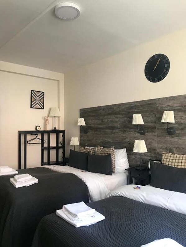 Une chambre d’hôtel avec deux lits, une tête de lit en bois, des lampes de chevet, une horloge murale et une petite table avec une lampe et un objet décoratif.