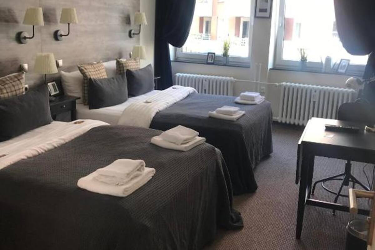 A hotel room with two beds, a desk, a clock, and a window with curtains.