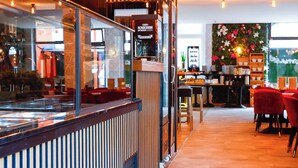 Un restaurante moderno con mostrador, sillas rojas, luces colgantes y suelo de madera.