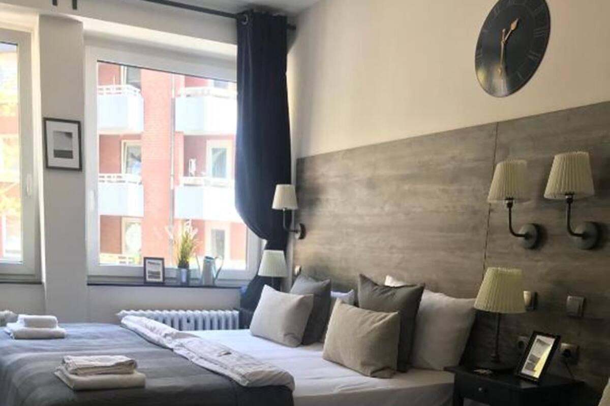 A hotel room with two beds, a clock, and a window with curtains.