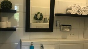 A bathroom with a white sink, a black-framed mirror, a towel rack with towels, and a shelf with toiletries. - Hamburg Room (Hamburg)