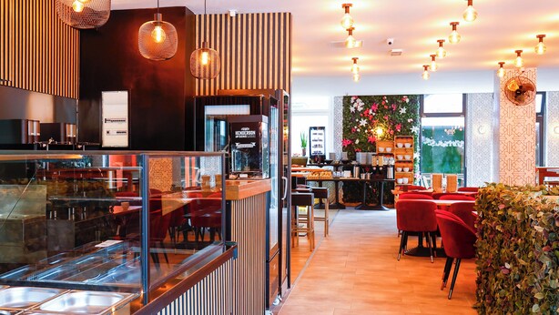 Un restaurante moderno con zona de bufé, sillas rojas y lámparas colgantes.