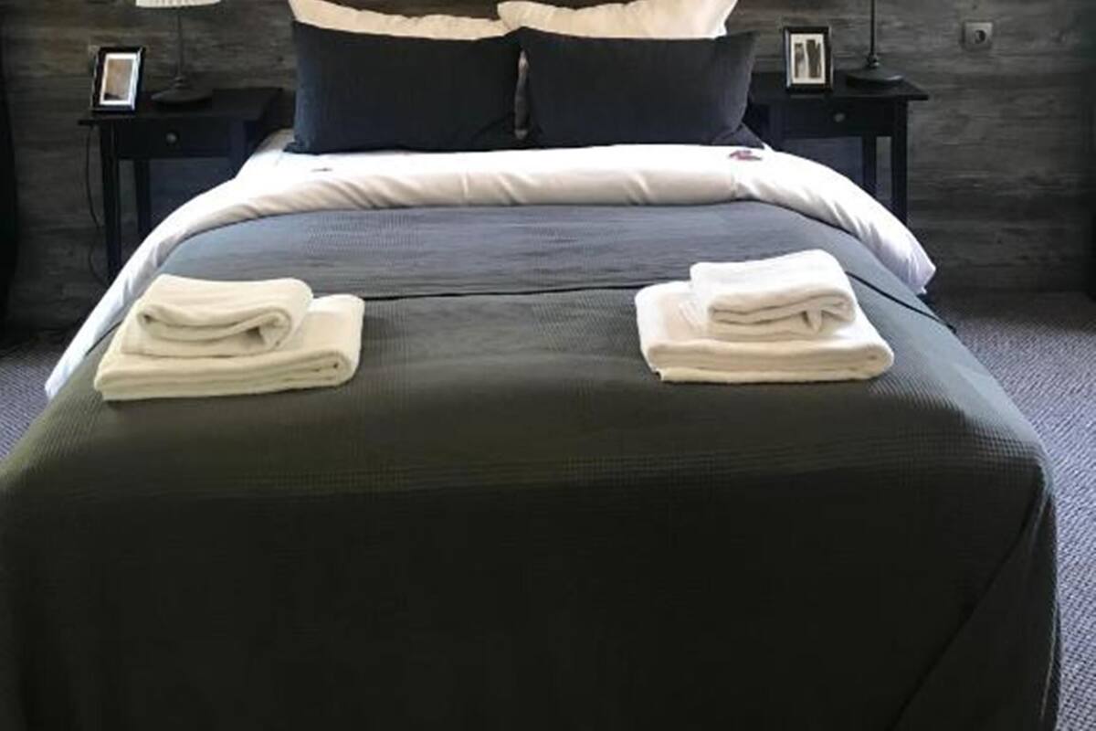 A modern bedroom with a dark wood headboard, a round black clock, two bedside lamps, and neatly folded towels on the bed.