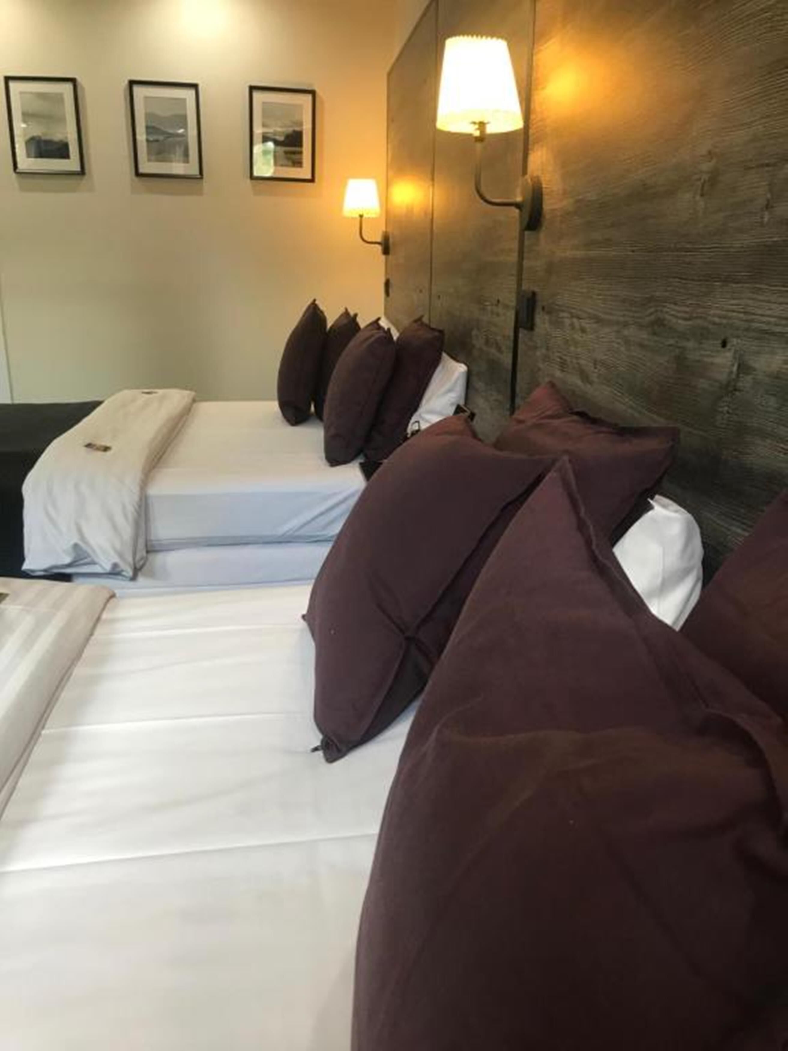 Ein Hotelzimmer mit einem großen Bett, vielen Kissen, einem Kopfteil mit Wandlampen und gerahmten Bildern an der Wand.