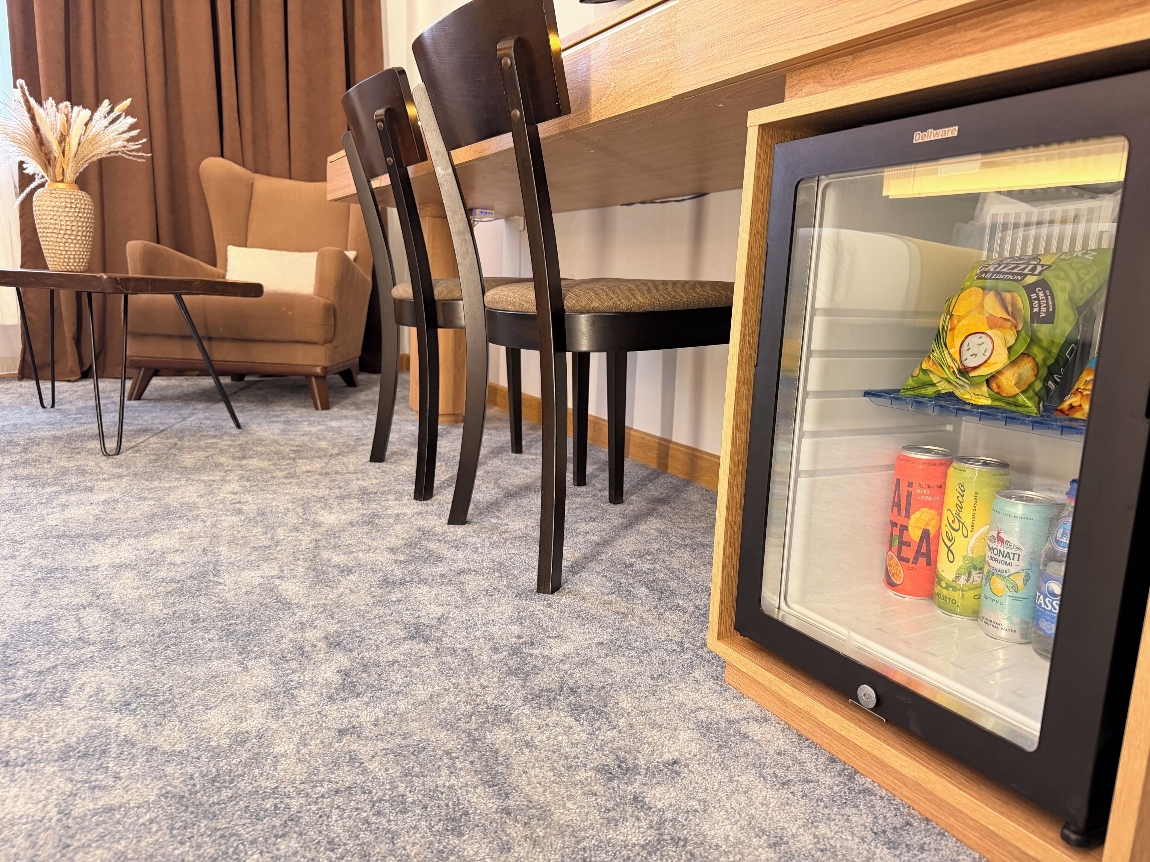 Une chambre dotée d’un coin salon, d’un réfrigérateur rempli de collations et de boissons, et d’un vase contenant des plantes séchées.