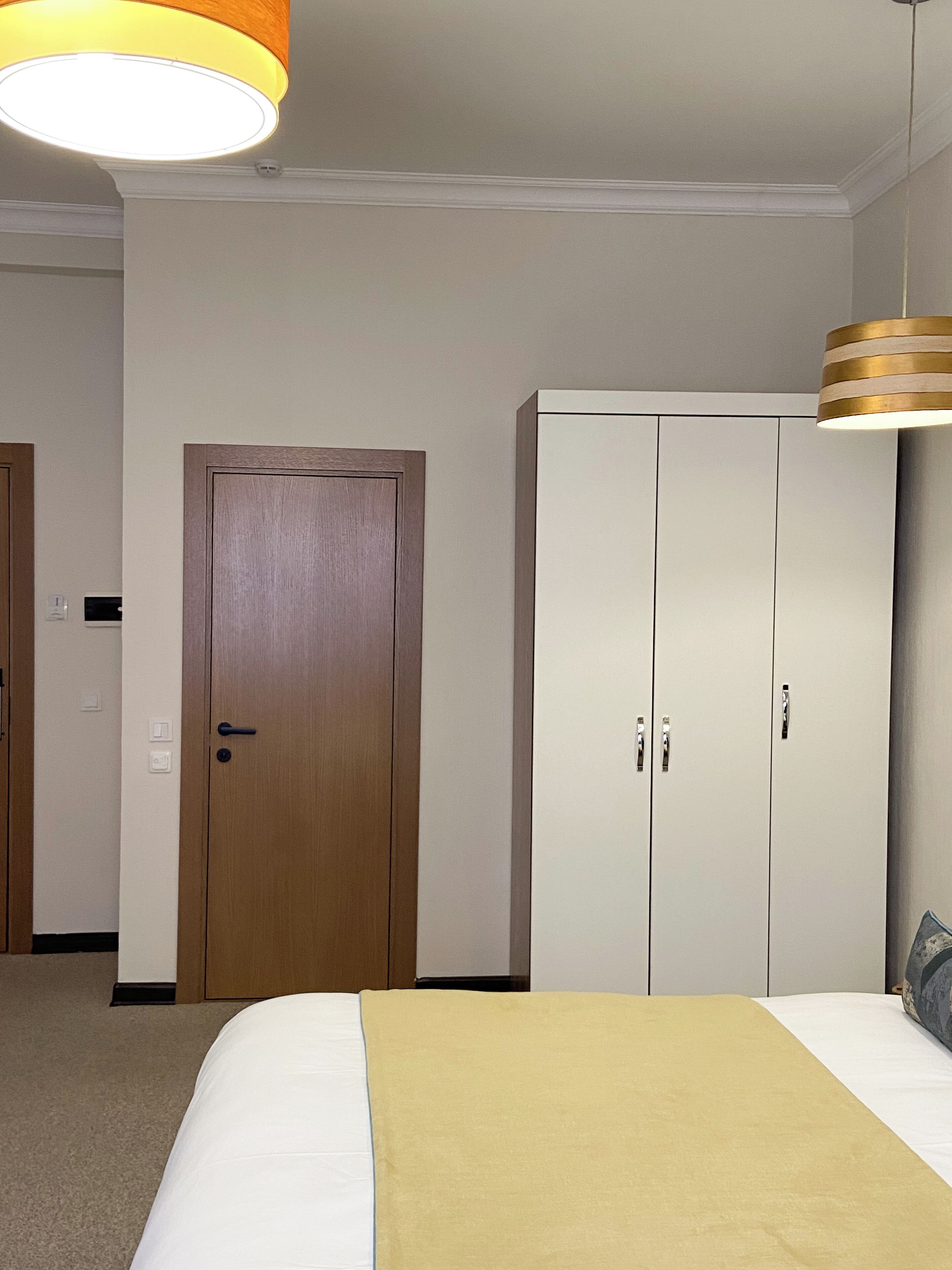 Een hotelkamer met een bed, een kledingkast, een deur en een plafondlamp.