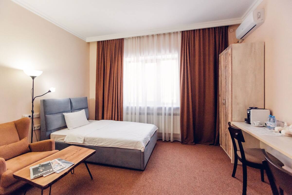 A hotel room with a bed, a desk, a chair, a lamp, and a wardrobe.