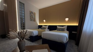 A hotel room with two beds, a coffee table with a laptop and a cup, a vase with dried plants, and a painting on the wall. - Keremet Hotel (Almaty)
