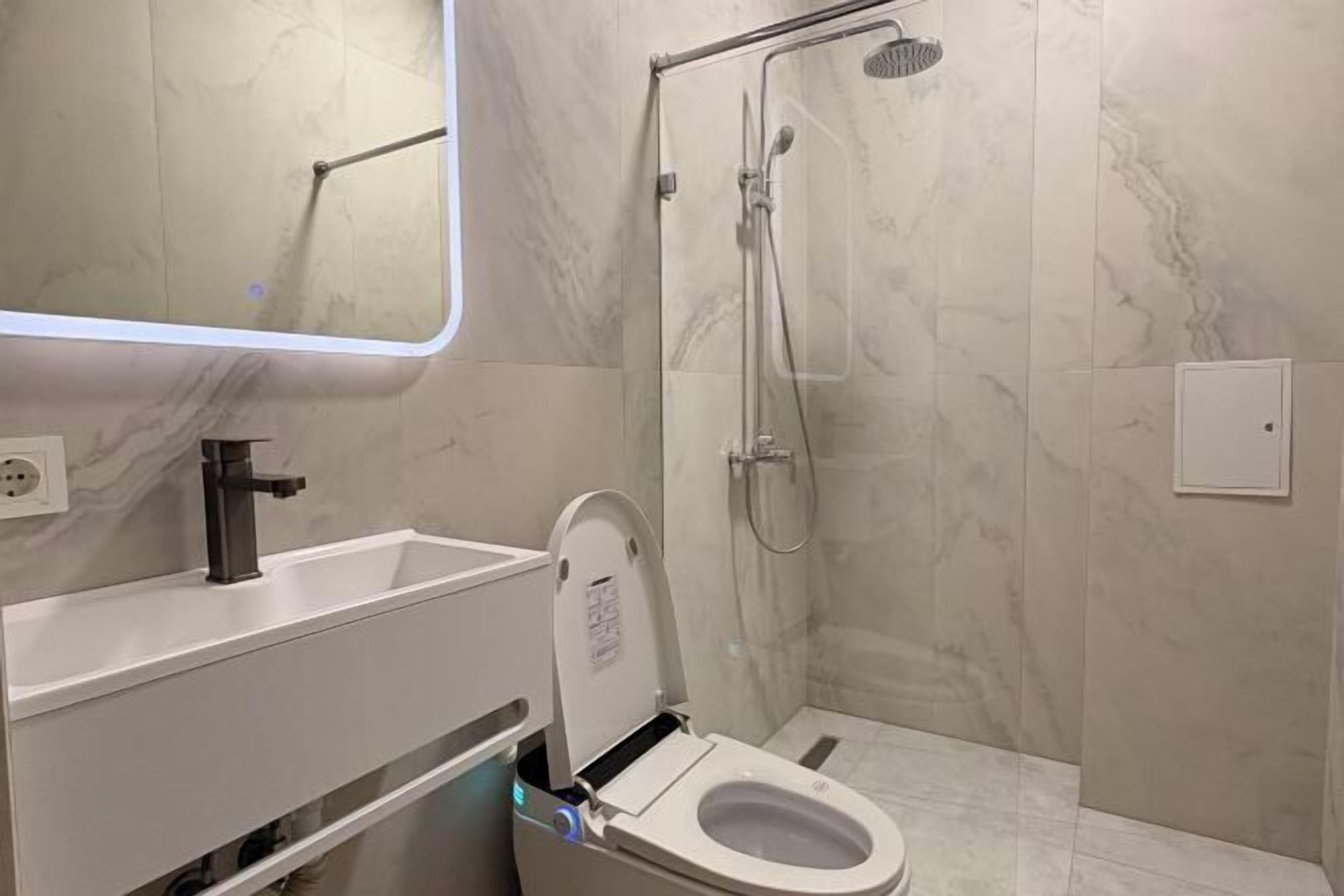 A bathroom with a toilet, sink, mirror, and shower.