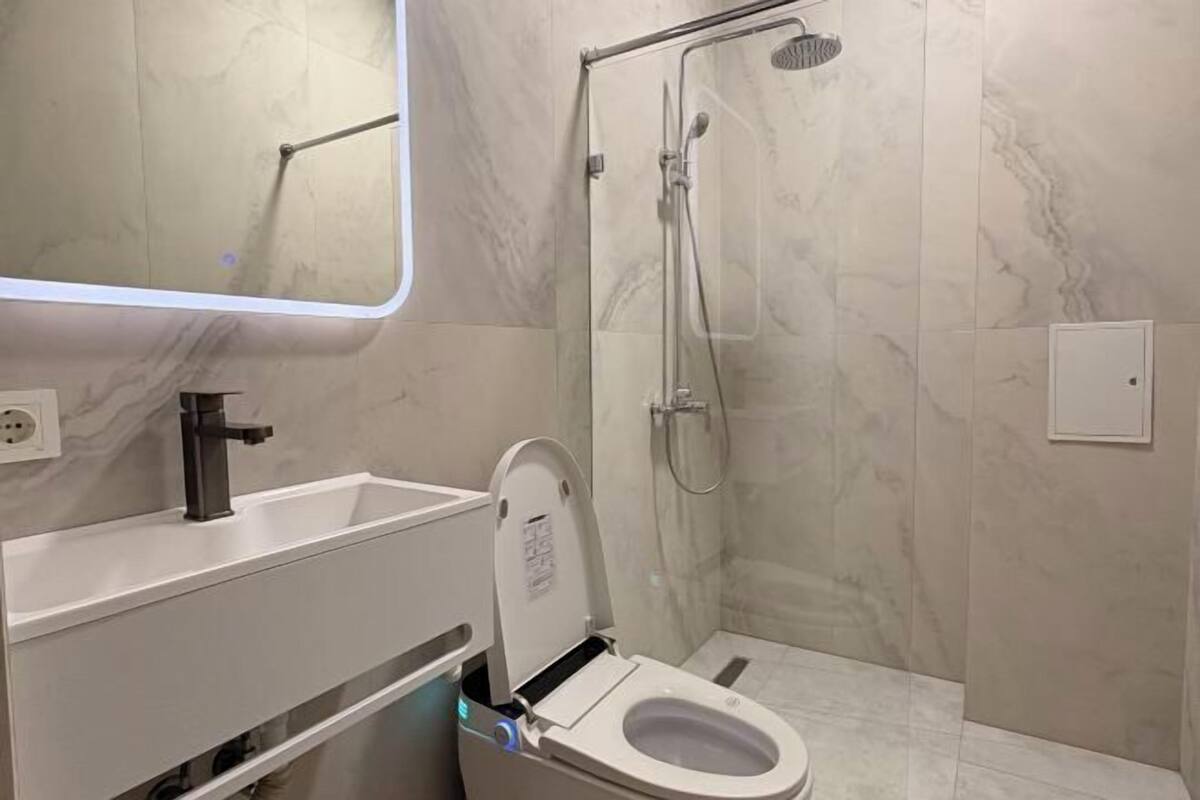 A bathroom with a toilet, sink, mirror, and shower.
