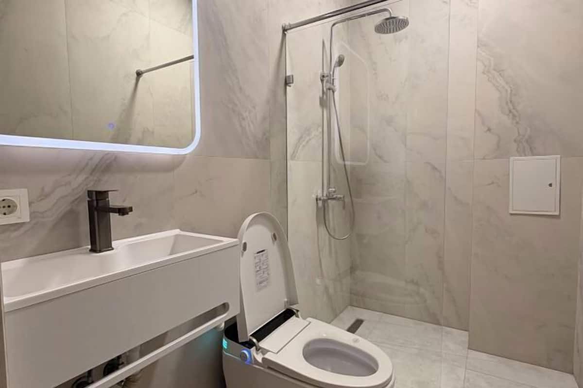 A bathroom with a toilet, sink, mirror, and shower.