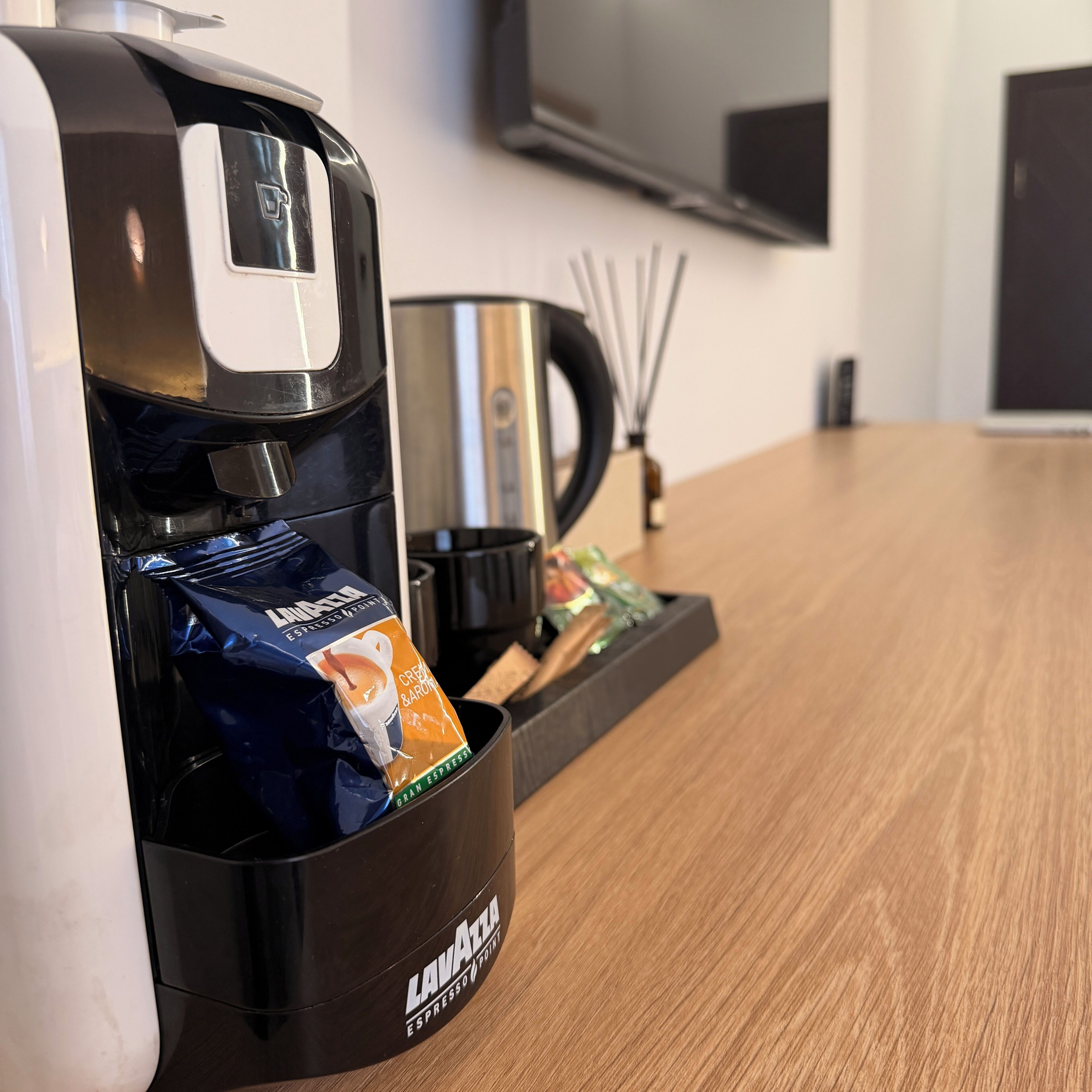 Eine Kaffeemaschine mit eingefügter Kapsel, eine schwarze Tasse und ein Tablett mit Löffel und kleiner Behälter.