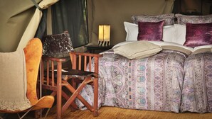 Une pièce aménagée avec une tente, un lit, une chaise en bois et une table de chevet avec une lampe.