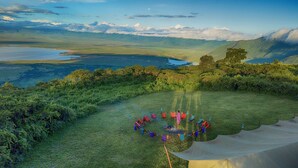 Un ensemble de chaises et de tables aux couleurs vives, disposées en cercle sur une pelouse, avec en arrière-plan un lac et des montagnes.