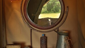 Un meuble-lavabo de salle de bain avec un miroir rond, deux lampes fixées au mur, un seau en métal, un distributeur de savon et un petit panier en osier.