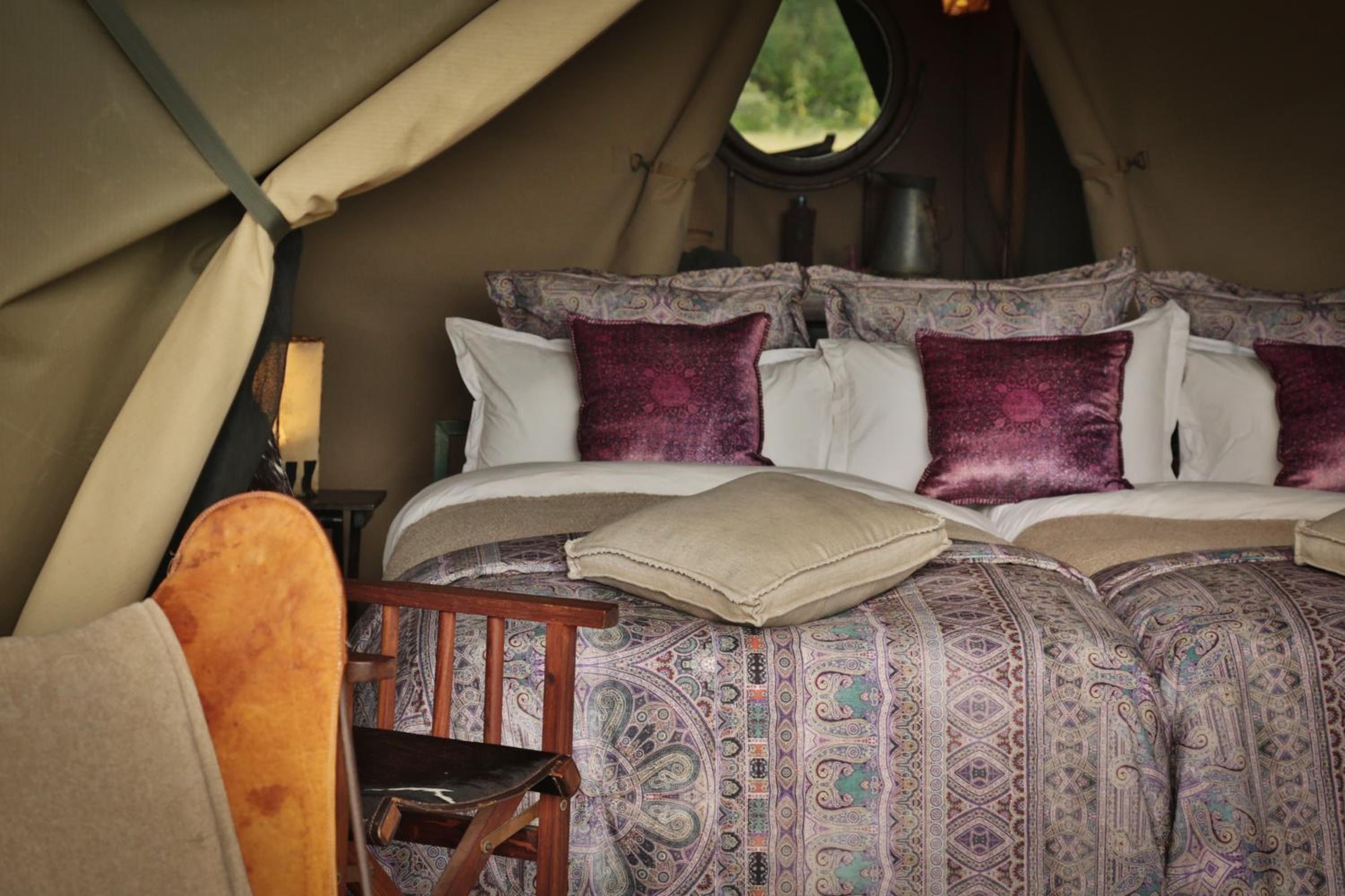 A tented room with a bed, pillows, a chair, and a window.