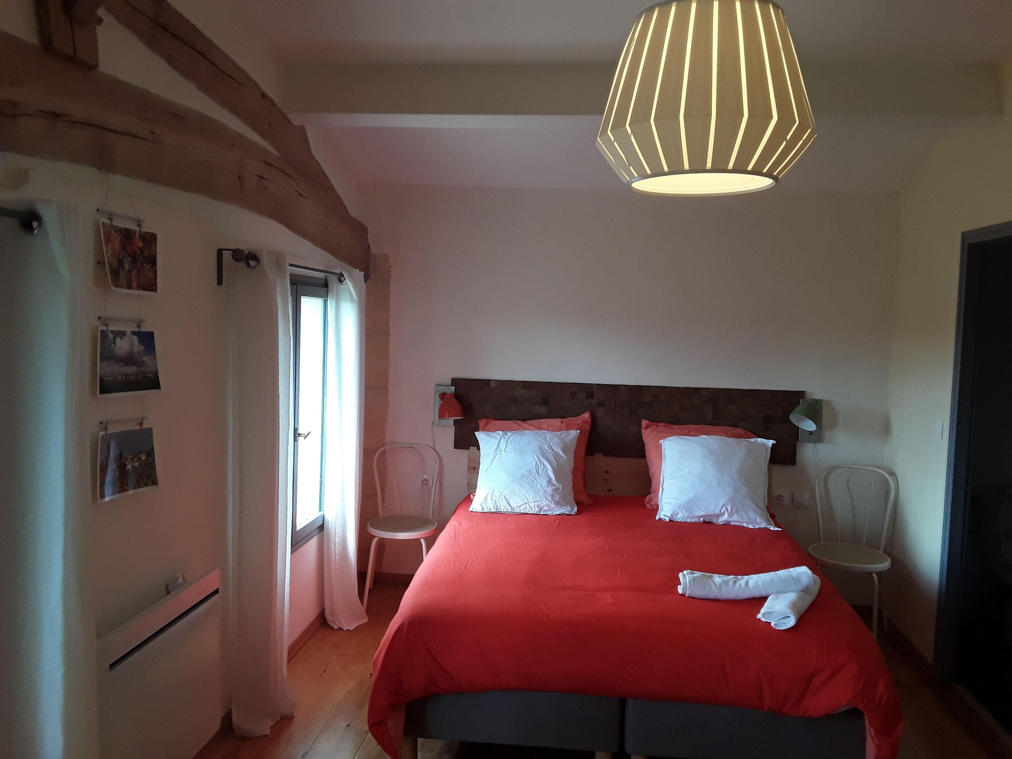 Ein Schlafzimmer mit einem hölzernen Kopfteil, einer roten Bettdecke, weißen Kissen und einer Hängelampe.