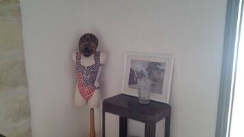 Ein Zimmer mit einem Holzstuhl, einem kleinen Tisch mit einem Glas und einem gerahmten Bild an der Wand.