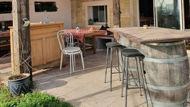 Un patio al aire libre con mesa y sillas de madera, una barra y un barril grande.