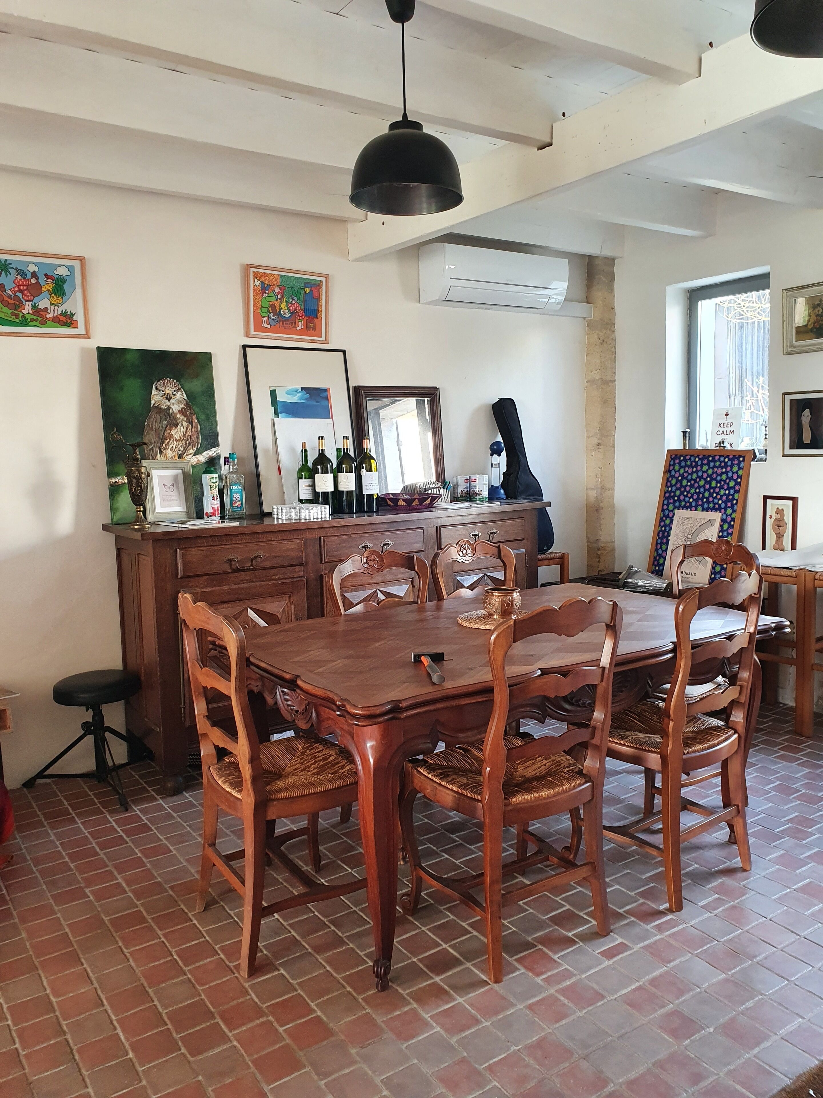 A dining area with a wooden table and chairs, a bar counter with bottles, and artwork on the walls.