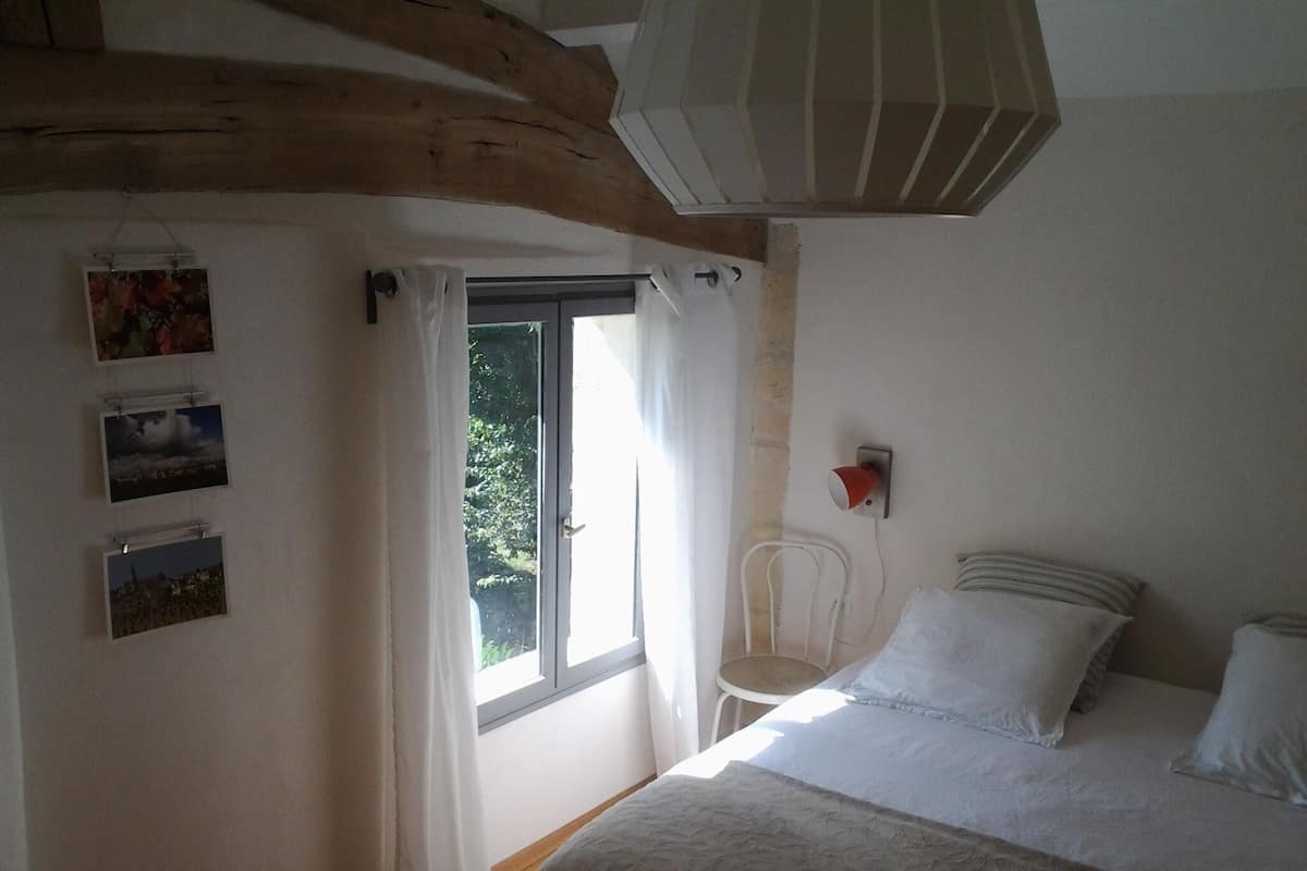 A bedroom with a bed, a window with curtains, a chair, and wall-mounted pictures.