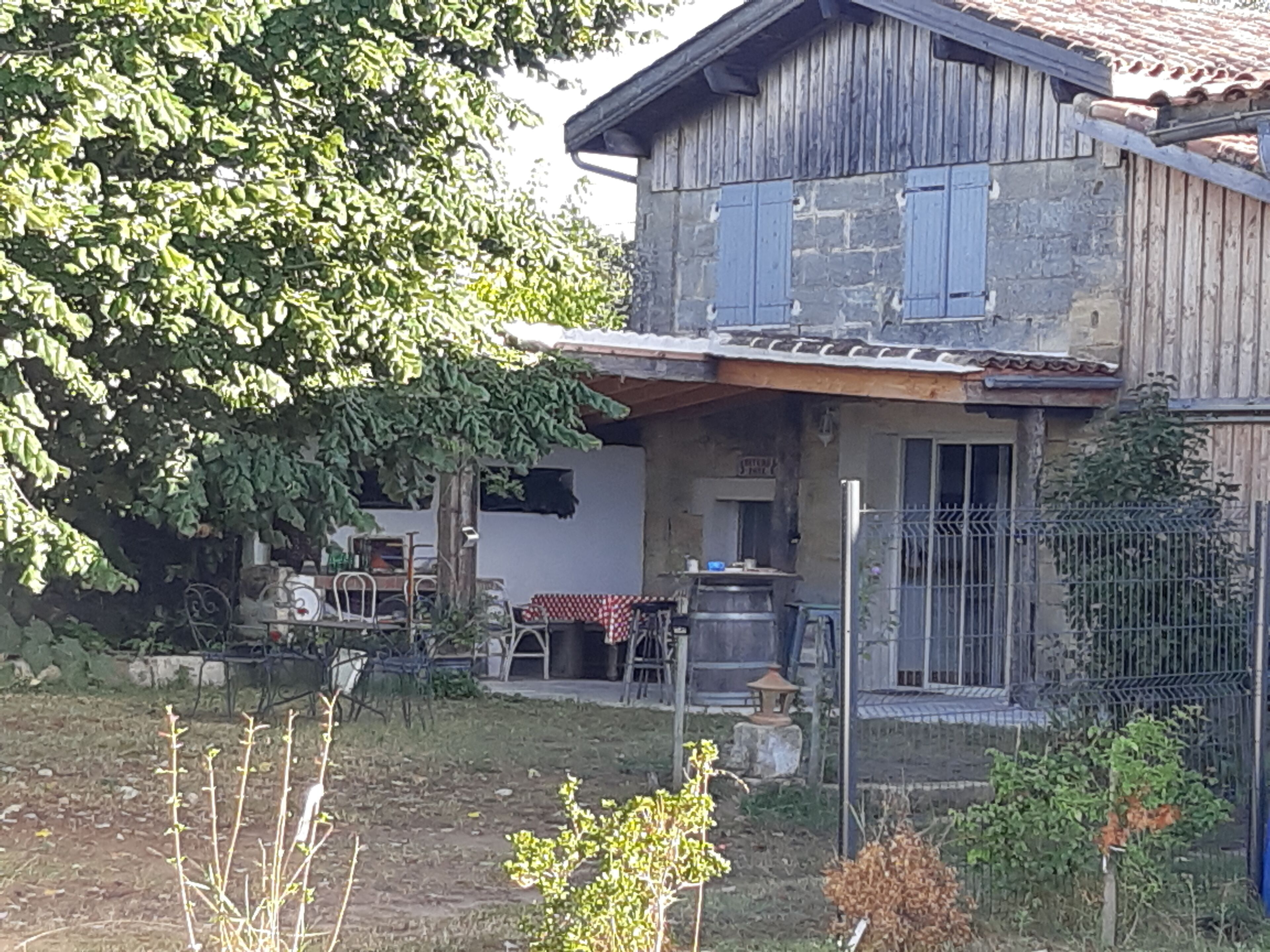 A rustic two-story house with a stone facade, a wooden porch, and a metal gate.