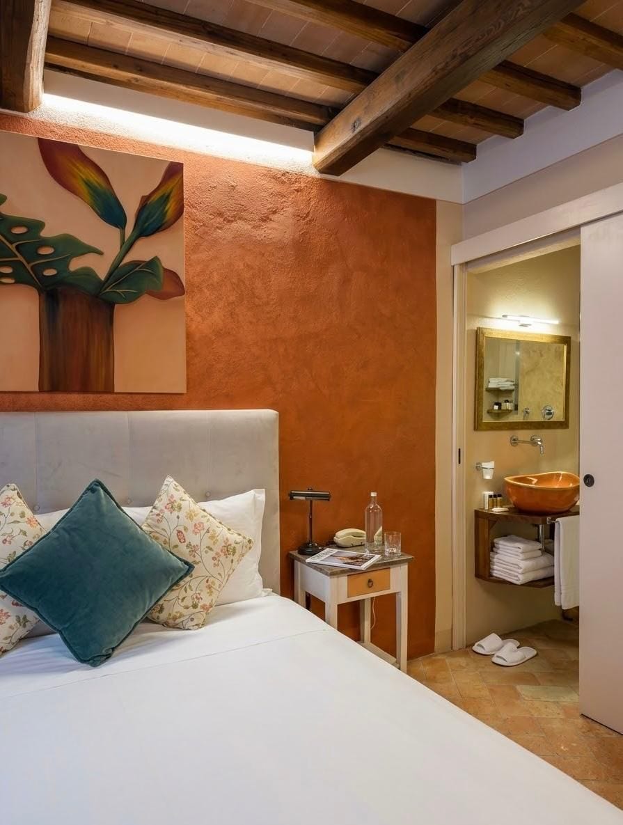 Une chambre à coucher comprenant un lit, des oreillers, une table de chevet, une commode, une salle de bain avec un lavabo, un miroir et des serviettes.