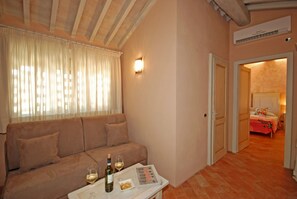 A cozy room with a sofa, a table with wine glasses and a bottle, and a door leading to a bedroom. - Molino di Foci (San Gimignano)