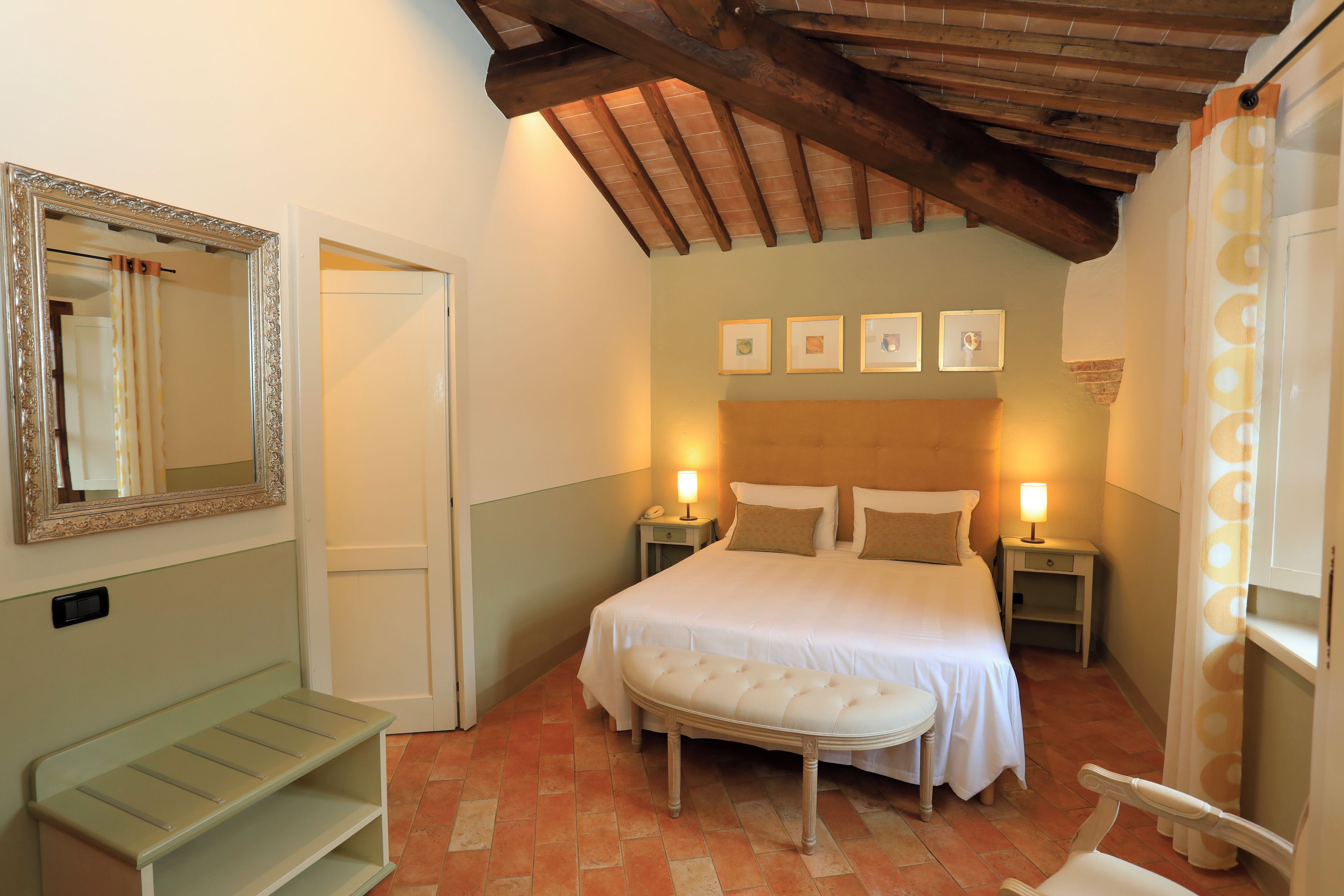 A bedroom with a bed, bedside tables, a bench, a mirror, and framed pictures on the wall.
