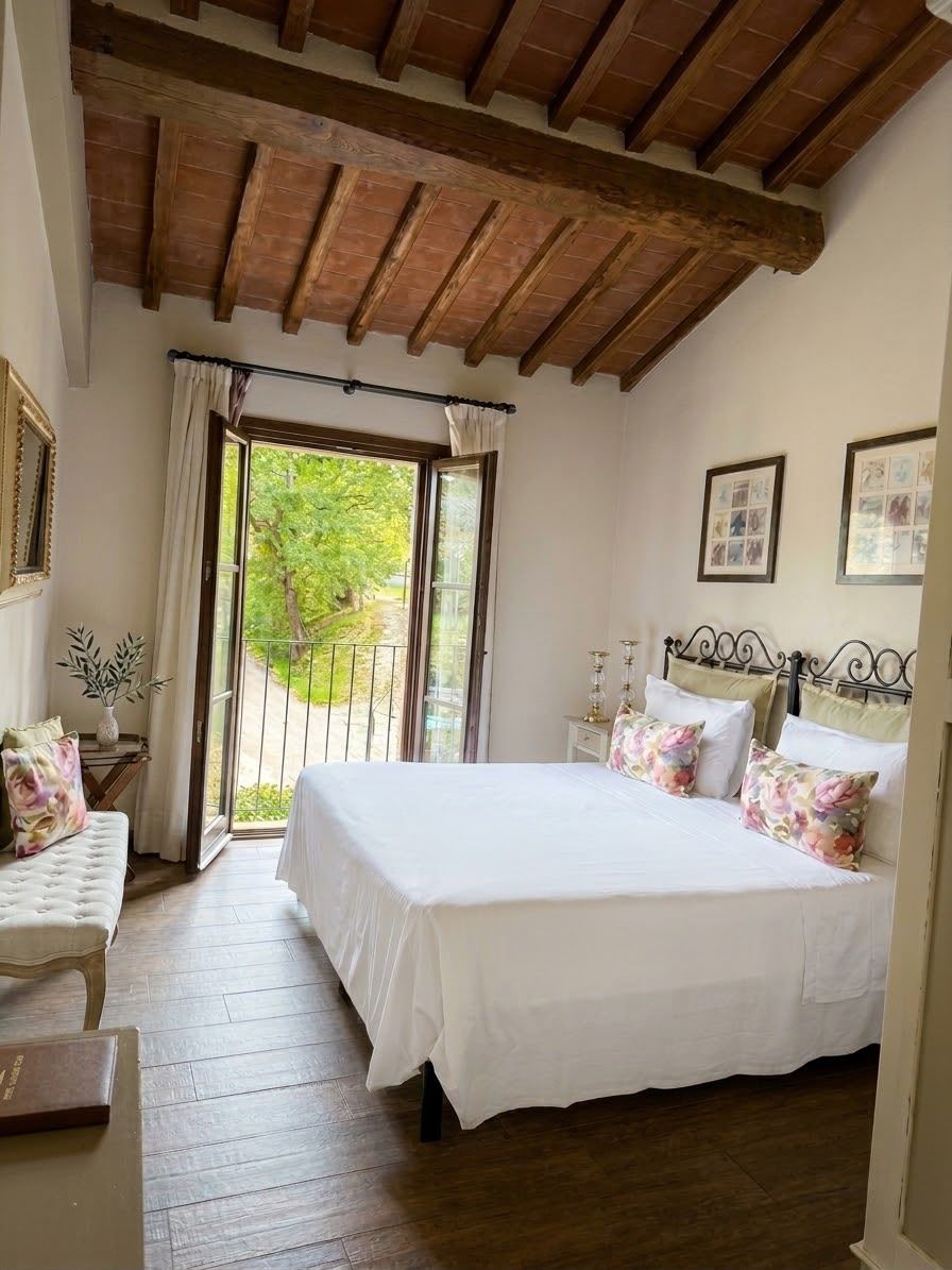 Ein Schlafzimmer mit einem großen Bett, einer Bank, einem Nachttisch und einem Balkon mit Vorhängen.