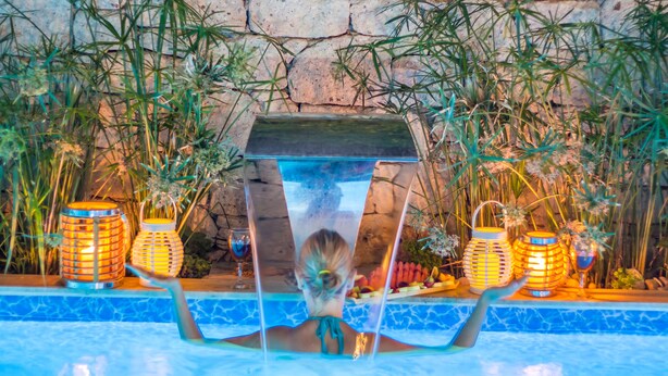 Un espace piscine avec une eau claire, entouré de murs en pierre et de plantes en bambou.