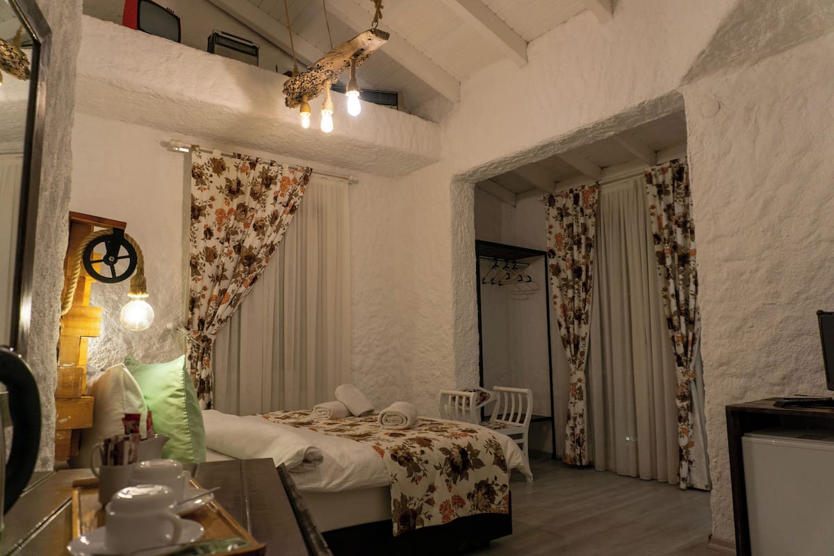 A bedroom with a bed, a chair, a desk with a computer, and a mirror.