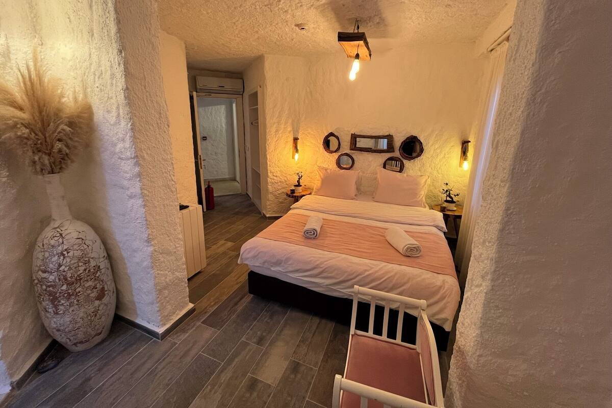 A cozy bedroom with a bed, bedside tables, a wall-mounted light fixture, and a large vase.