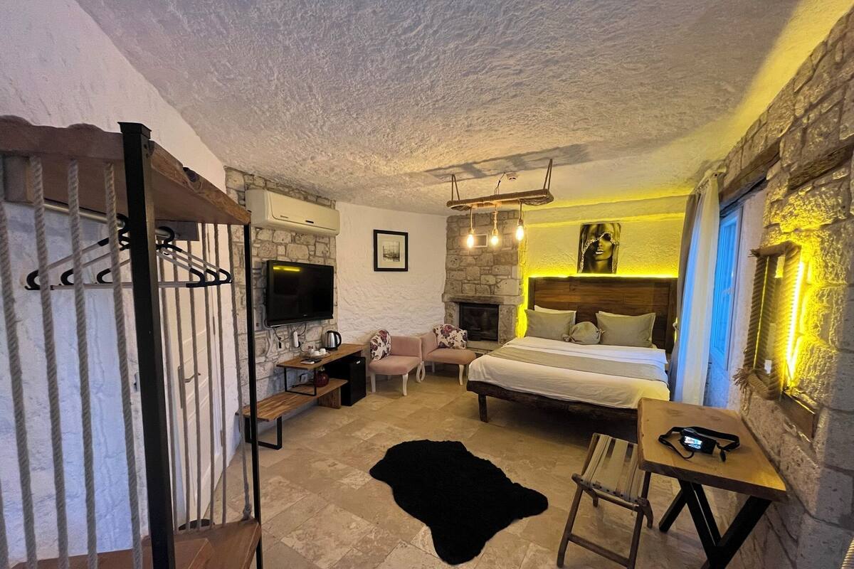 A cozy bedroom with a stone fireplace, a bed, a desk, and a TV.